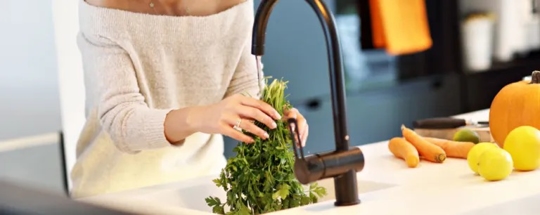 Person washes vegetables at a kitchen sink.