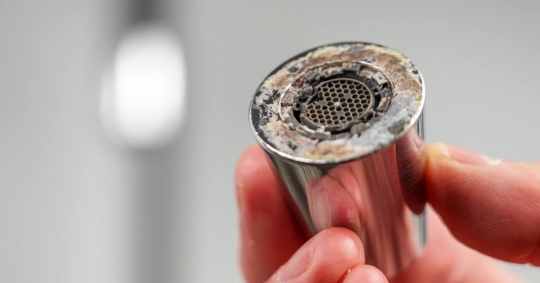 A plumber is holding a chrome faucet aerator with lime scale in kitchen