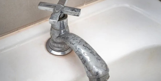 A tarnished metal faucet is mounted on a white sink.