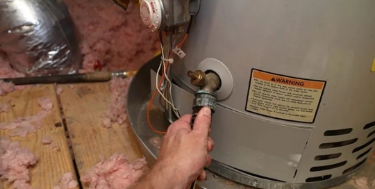 A hand is connecting a hose to a spigot on a water heater