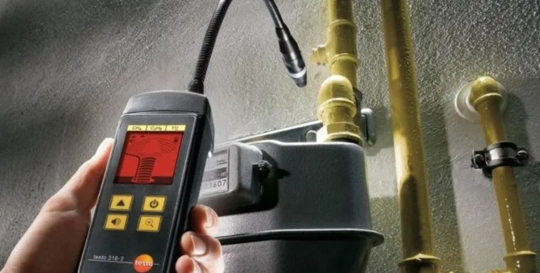 A person is using a gas leak detector on pipes and a meter.