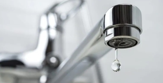 A chrome faucet is dripping a clear water droplet.