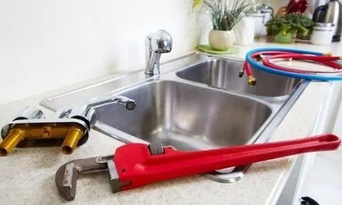 A wrench, faucet, and new plumbing lines are featured on a sink.