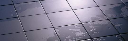 Wet, dark gray square tiles are arranged to create an abstract floor background.