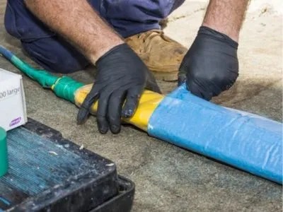 A person wearing gloves is wrapping a thick cable with blue tape.