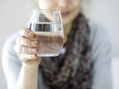 A woman holds up a glass of water in front of her face.