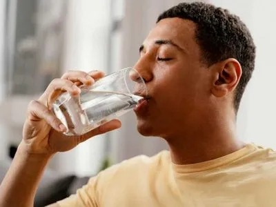 A man is drinking water while his eyes are closed
