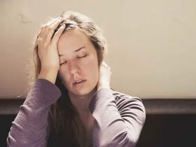 A woman with eyes closed holds her head with a stressed expression.
