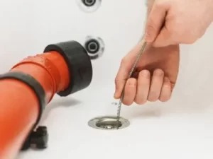 A person is using a hook tool to unclog a bathtub drain