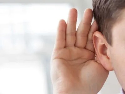 A person is cupping their hand to their ear, possibly listening intently.