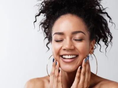 A woman with curly hair and large hoop earrings smiles with her eyes closed