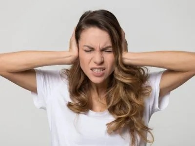 A woman with an irritated expression covers her ears with her hands.