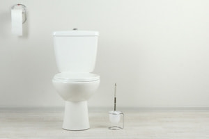A white toilet sits against a white wall with light grey flooring.
