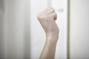 A pale-skinned fist is raised against a white wall.